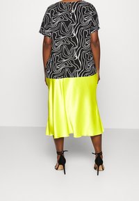 Halenka s černobílým vzorem a krátkými rukávy, doplněná lesklou neonově žlutou saténovou sukní a černými lodičkami na kotník.