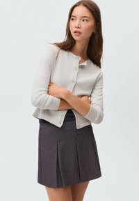 Cardigan gri deschis cu guler rotund, închidere cu nasturi și manșete côté, asortat cu o fustă plisată închisă la culoare. Textură netedă în întregime.