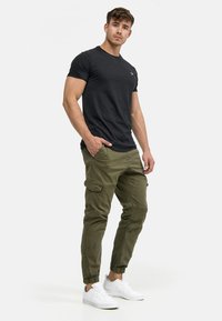 T-shirt noir à manches courtes avec un col rond, associé à un pantalon cargo vert olive avec des poignets élastiques et des poches latérales. Baskets blanches.