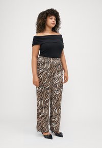 Μαύρη μπλούζα με ανοιχτούς ώμους, συνδυασμένη με καφέ και άσπρες φαρδιές παντελόνες με σχέδιο. Το μοντέλο φοράει μαύρες μυτερές γόβες. Επιφάνεια υφάσματος επίπεδη.