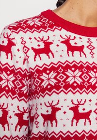 Roter und weißer Strickpullover mit Rentiermuster, Schneeflocken und geometrischen Formen, mit rundem Ausschnitt und gerippten Rändern.