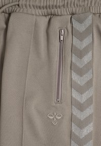 Beige Sportshorts mit elastischem Bund, seitlicher Reißverschlusstasche und einer strukturierten silbernen Chevron-Musterung an der Seite. Besticktes Logo-Detail.