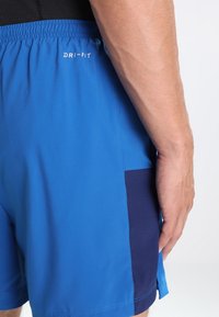 Pantalones cortos deportivos azul con la marca Dri-Fit, que cuentan con un panel azul marino en el costado. La tela tiene una textura suave y áreas ventiladas.