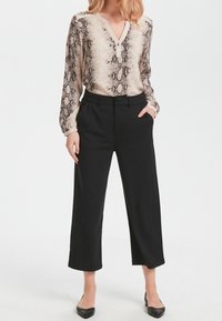 Hedvábná blůza s dlouhým rukávem v béžovém a černém hadím vzoru, spárovaná s černými zkrácenými kalhotami. Blůza má výstřih do V a ozdobné knoflíky.