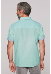 Camicia verde menta con maniche corte, polsini a righe a contrasto e dettaglio sulla spalla posteriore. Tessuto morbido, colletto con bottoni e orlo curvo.