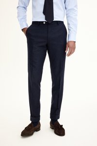 Marinblå byxor med skräddarsydd passform, tillverkade av ett texturerat tyg. Har knappstängning och uppvikta fållar, kombinerade med mörkbruna loafers.