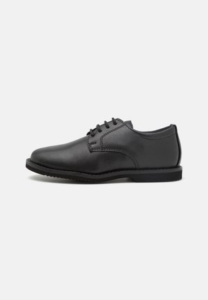Zapato oxford negro de cuero con cordones, punta redondeada y suela plana, mostrado de lado sobre un fondo blanco liso.