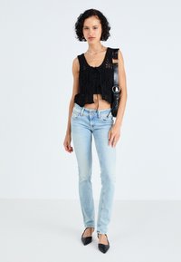 Fekete horgolt crop top, elöl megkötő részlettel, világoskék slim-fit farmernadrággal és fekete, hegyes orrú lapos cipővel párosítva.