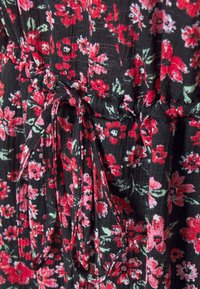 Tissu noir avec motif floral rouge et rose, présentant un cordon de serrage noué créant une texture froncée.