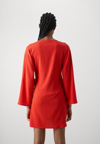 Vestido rojo texturizado con mangas largas y corte recto, que presenta un escote redondo y un acabado suave. Vista trasera mostrada.