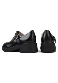Chaussures compensées en cuir noir avec bout arrondi, dotées d'une boucle latérale, d'un talon surélevé et d'une semelle en caoutchouc texturée pour une meilleure adhérence.