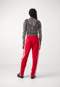 Top de mangas longas com padrão de zebra em preto e branco, combinado com calças de treino vermelhas com riscas laterais brancas e fechos de botão. Sapatos planos.