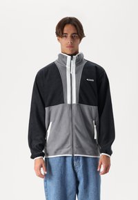Fleece jacket in gray and black, featuring a high collar, full zipper, and side pockets. Accented with white trim and a logo on the chest.