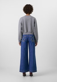 Grijze hoodie met geribbelde manchetten, gecombineerd met wijde blauwe denim jeans met kenmerkende gebogen achterzakken en een kettingdetail.