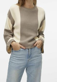 Pull-over en maille présentant des rayures horizontales beige et crème, une texture côtelée, des manches larges et un col rond, associé à un denim clair.