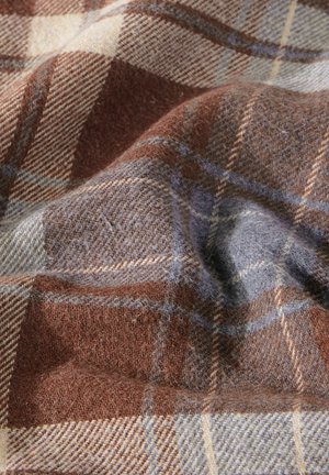 Hnědý a modrý kostkovaný textil s měkkým, texturovaným povrchem a chlupatým dokončením, zvýrazňující vzájemně se překrývající linie a čtverce různých velikostí.