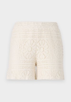 Kremkrāsas mežģīņu šorti ar sarežģītiem ziedu rakstiem un elastīgu jostasvietu, demonstrējot tekstūras, atvērtu adījumu.