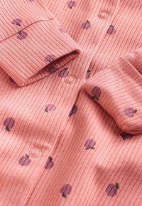 Rosa ribbad barnonesie med lila fruktmotiv, framknappning och ärmslut. Mjuk, texturerad tyg.