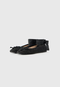 Ballerines noires en tissu texturé avec un subtil éclat. Détail en nœud à l'avant, rubans à la cheville et design à bout pointu.