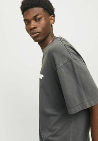 Grå oversized T-shirt med korte ærmer og rund halsudskæring. Har subtile syninger og et lille hvidt logo på forsiden.