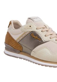 Beiga och bruna Pepe Jeans-sneakers med texturerade paneler, beiga snören och logotyp på sidan och på tungan, vinklad för att visa yttersidan.