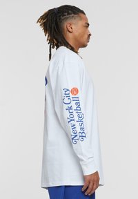 Langarm weißes Baumwoll-T-Shirt mit blauer Aufschrift "New York City Basketball" auf einem Ärmel und Logo auf der Brust. Einfaches, lässiges Design.
