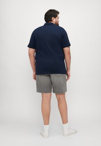 Polo shirt bleumarin, cu mâneci scurte, și o croială dreaptă, asortat cu pantaloni scurți din denim gri. Pantofi sport albi și șosete ribbate până la gleznă completează look-ul.