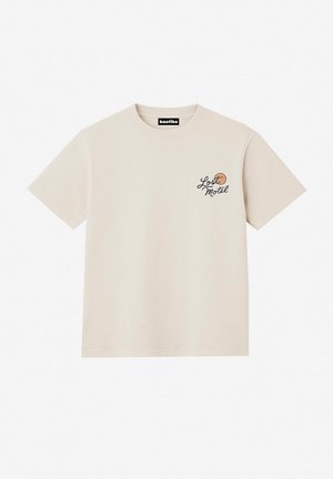 Bēšas krāsas īsām piedurknēm T-krekls ar uzrakstu "Lost Motel" un nelielu gaiši brūnu apli kreisās krūtis daļā, apaļu kaklu un Kaotiko zīmola etiķeti apkaklē.