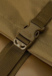 Chiusura di una borsa in nylon marrone con fibbia in plastica e logo impresso. Texture visibile e dettagli di cucitura aumentano la durata.