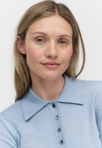 Ljusblå stickad tröja med krage och fem metallknappar fram. Mjuk textur och figurnära design. Enkel och ren look.