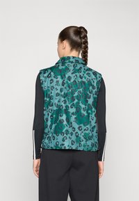 Gilet en imprimé léopard vert avec un design sans manches, fabriqué en tissu lisse, présentant un col et un ourlet inférieur élastique.