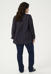 Dark navy long-sleeve blouse with a flowy cut, paired with slim-fit dark blue jeans. Smooth texture, no visible patterns, and back view.