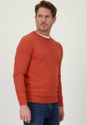 Rode crewneck trui van gebreid materiaal, met lange mouwen en een aangesloten taille, gecombineerd met donkerblauwe spijkerbroeken.