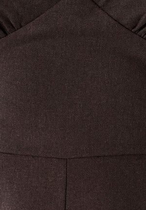 Tamno smeđi teksturirani materijal s vidljivim šavovima i presavijenim detaljem nabora blizu gornjeg ruba.