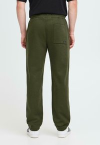 Olivgrüne Jogginghosen mit elastischem Bund, Taschen auf der Rückseite und schmal zulaufenden Beinen. Hergestellt aus weichem Material mit einer glatten Textur.