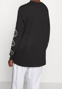 Czarna koszula z długim rękawem wykonana z bawełny, z białymi graficznymi wzorami na rękawach. Okrągły dekolt i luźny krój.