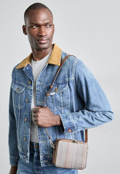 Denim jaka ar brūnu korduroja apkakli, pelēka krekla apakšā un neliela svītrainā pleca soma ar brūnu siksnu.