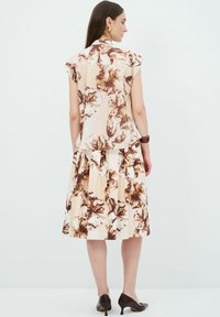 Set di abito floreale in tessuto beige con motivi floreali marroni, maniche a sbuffo, corsetto aderente e gonna a campana. Scarpe con tacco alto marroni.