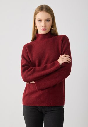 Pulover cu guler înalt burgund într-un tricot moale, texturat. Dispune de mâneci lungi, căzute și o croi lejer. Purtați cu pantaloni negri.