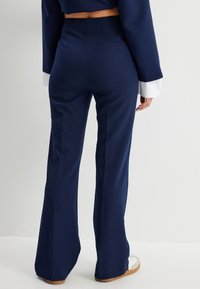 Pantalons évasés bleu marine avec une texture lisse, dotés de poches arrière et d'une taille haute. Assortis avec des poignets blancs aux manches.