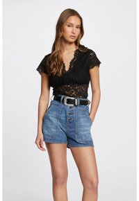 Top in pizzo nero con maniche corte, abbinato a shorts in denim blu a vita alta con bottoni frontali e una cintura nera con fibbia argentata.
