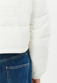 Witte pufferjack met een gequilt textuur en een cropped ontwerp, gecombineerd met blauwe denim jeans met een achterzakdetail.