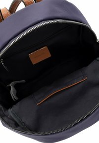 Marineblauer Rucksack mit braunen Lederelementen, ausgestattet mit einem Reißverschluss, geräumigem Innenraum und einer kleinen Innentasche zur Organisation.