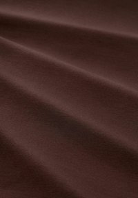 Brauner Baumwollstoff mit einer glatten Textur, der leicht gefaltet und zerknittert ist. Die Oberfläche wirkt weich und gleichmäßig mit einem konsistenten Farbton.