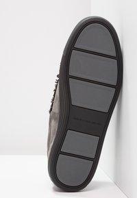 Scarpa in suede grigia con suola in gomma testurizzata, caratterizzata da una serie di motivi in rilievo per la presa e segmenti flessibili per la trazione.