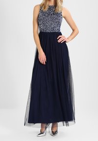 Navyblå maxiklänning med ett mönstrat liv och tylskjorta. Har hög krage och glittriga silverskor med hög klack.