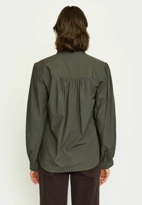 Blusa verde oliva a maniche lunghe con schiena arricchita, colletto a camicia, e tessuto morbido. Presenta maniche complete con polsini elasticizzati.