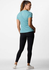Maglietta atletica turchese a maniche corte con un design aderente, abbinata a leggings neri. Le sneakers hanno una base bianca con accenti sottili.
