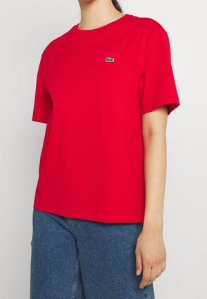 Czerwona bawełniana koszulka T-shirt z krótkim rękawem i okrągłym dekoltem. Posiada małe zielone logo Lacoste na piersi. Luźny krój.