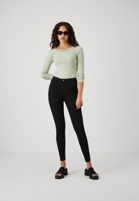 Light green ribbed long-sleeve top paired with black fitted jeans and chunky black slide sandals, set against a plain white background.